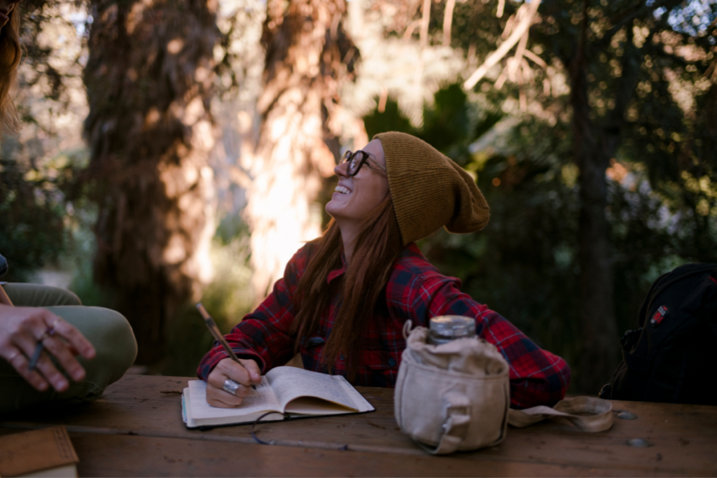 Una ragazza che ride mentre scrive il suo diario seduta nel bel mezzo della natura