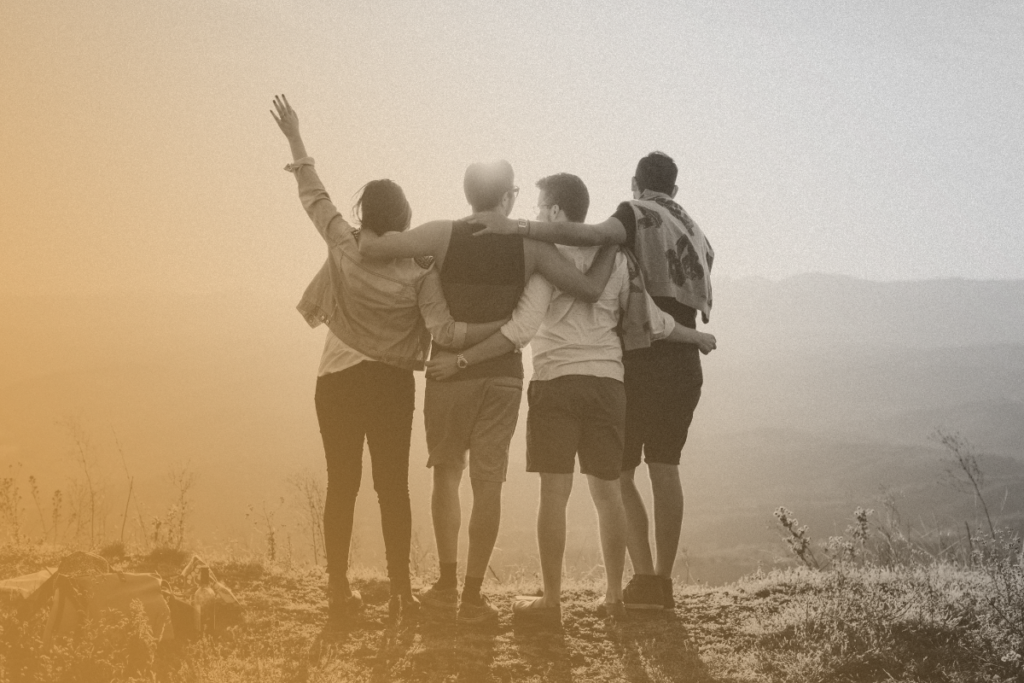4 persone felici di cultura ed etnie differenti stanno insieme con le mani le braccia rivolte verso l'alto guardando un panorama