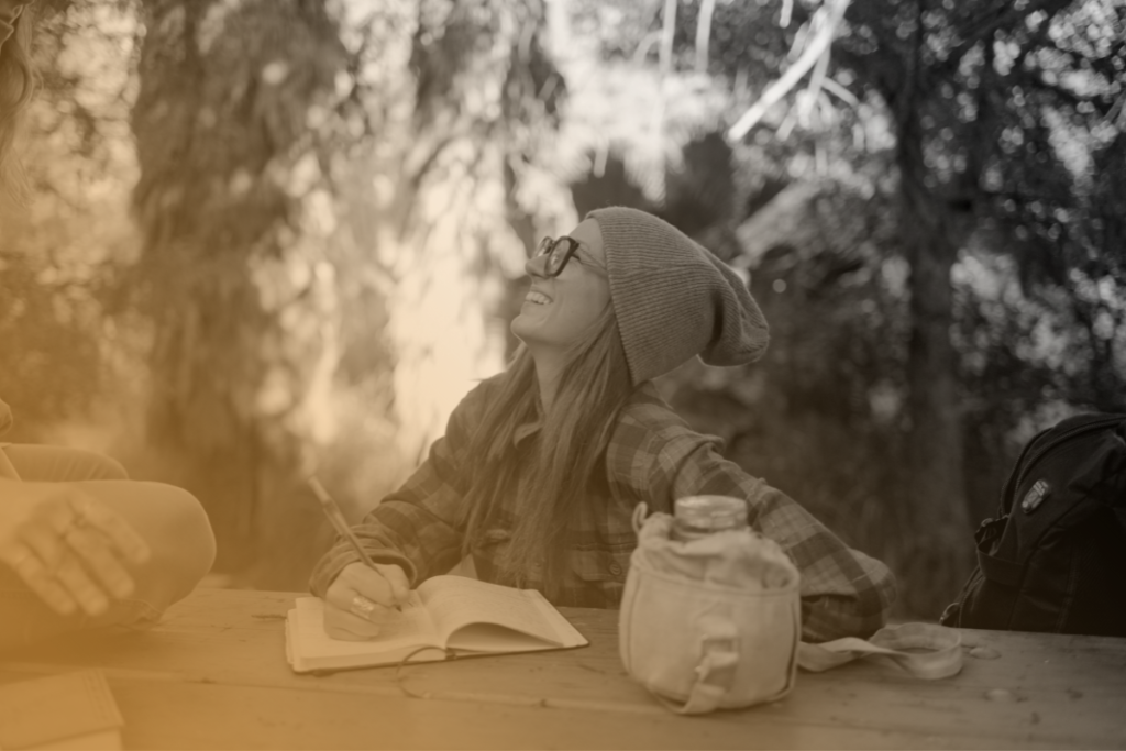Una ragazza che ride mentre scrive il suo diario seduta nel bel mezzo della natura