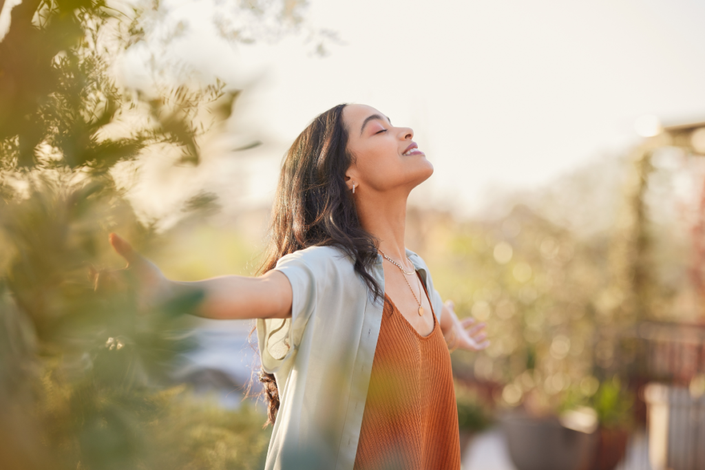 una ragazza con il viso rivolto verso il cielo, un bel sorriso e le braccia spalancate, si gode un momento di vera gratitudine. 