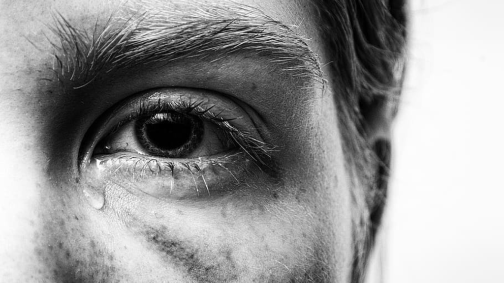 Un ragazzo piange in preda al burnout. Una foto in bianco e nero. in primo piano un occhio della faccia.
