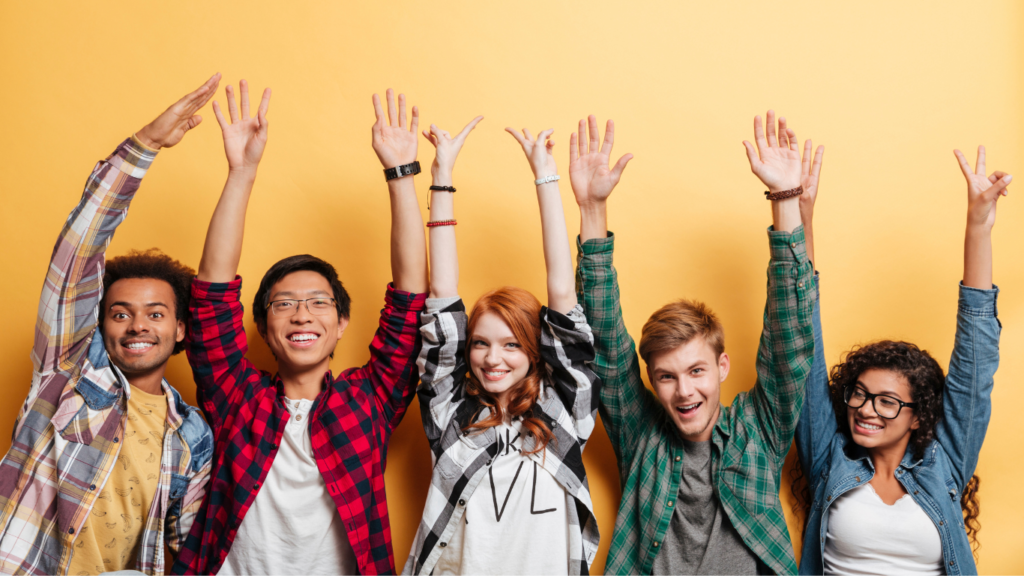5 persone felici di cultura ed etnie differenti stanno insieme con le mani le braccia rivolte verso l'alto. 